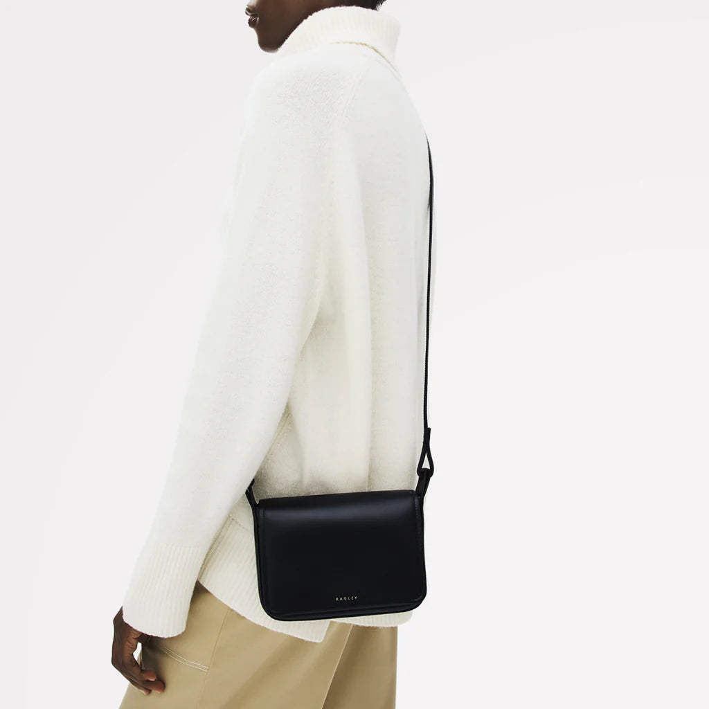 Person wearing a black crossbody bag with a plain background