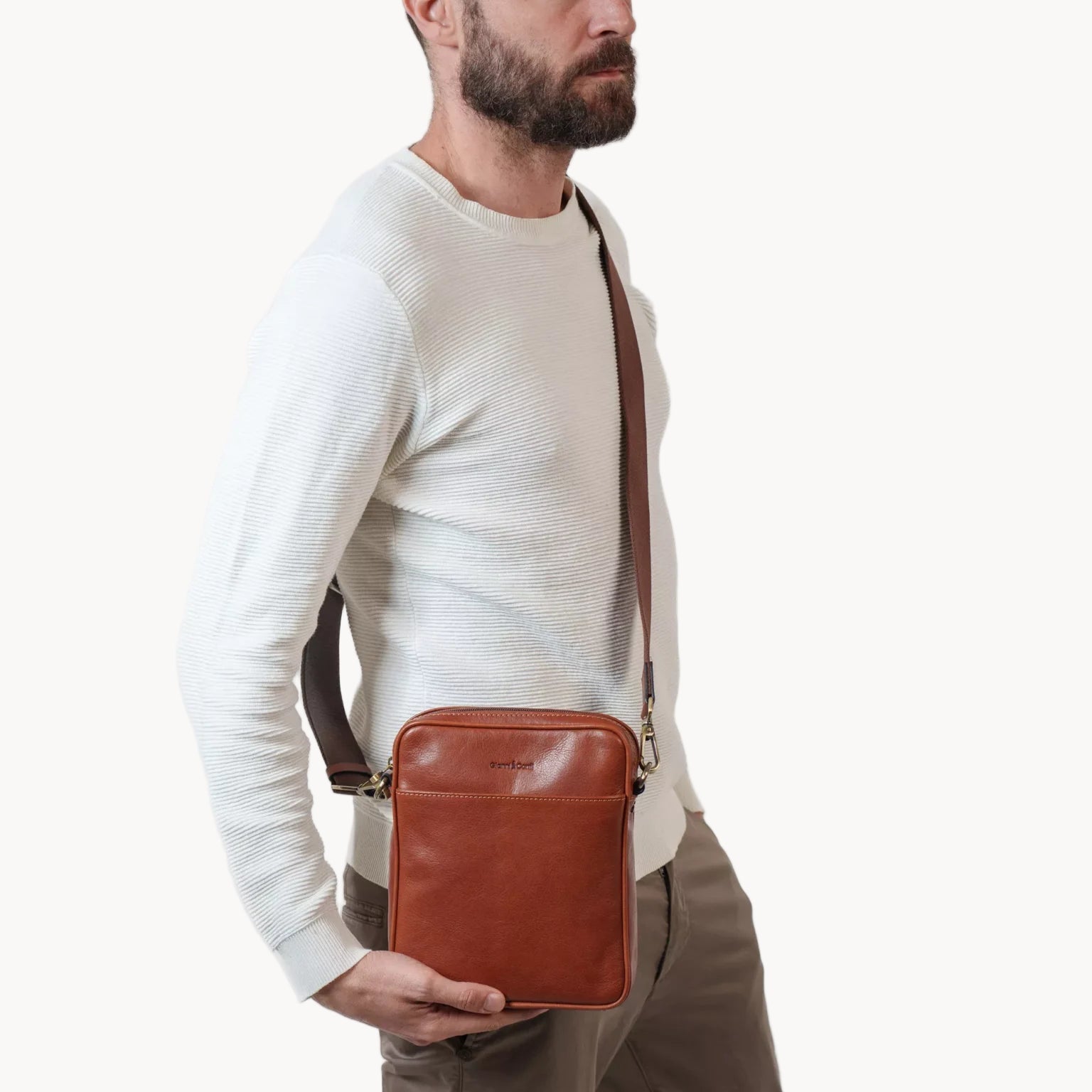 Man wearing a brown leather crossbody bag against a white background