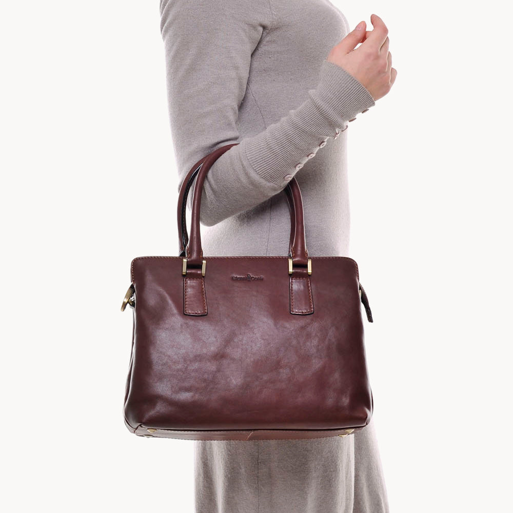 Brown leather handbag held by a person wearing a gray sweater on a white background