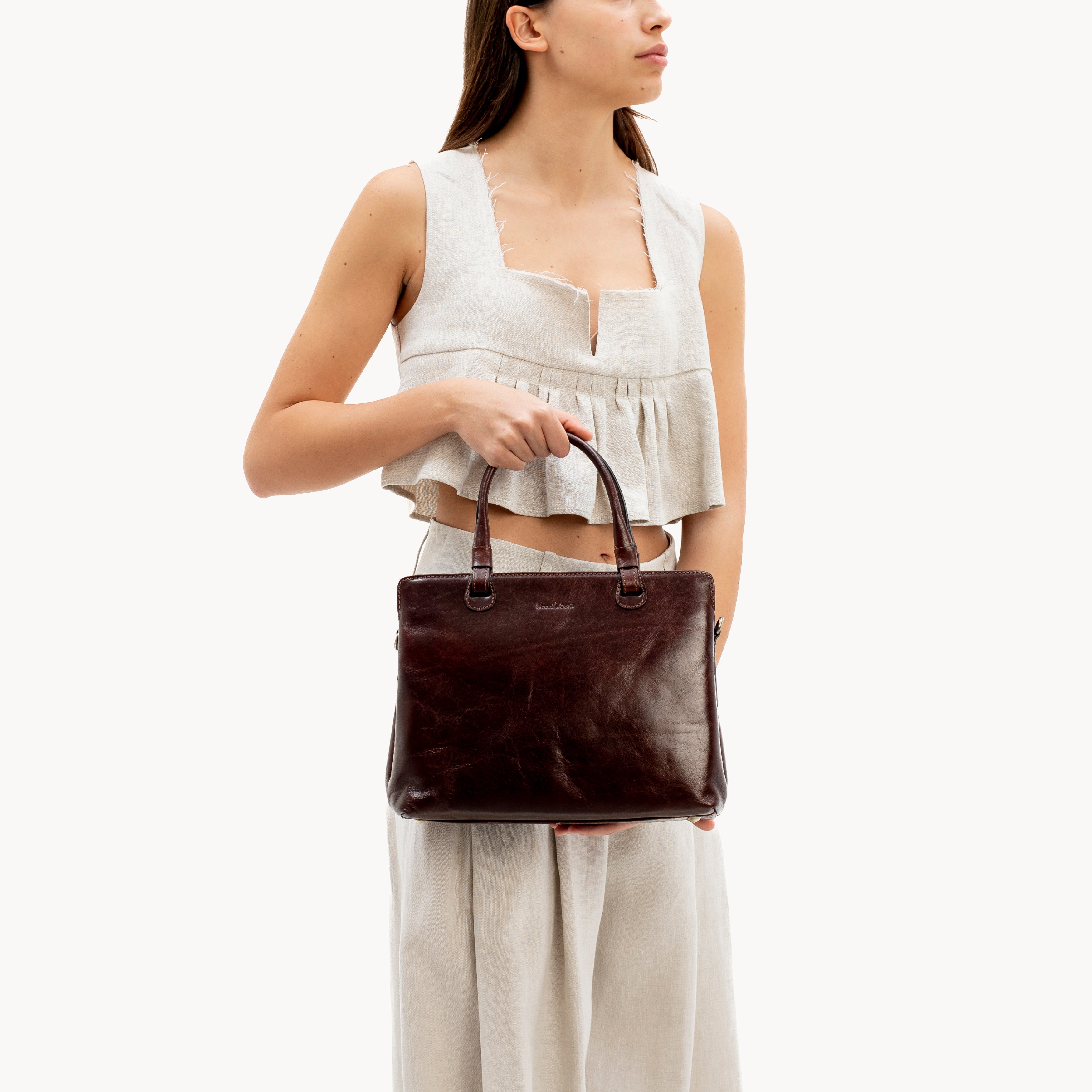Woman holding a brown leather handbag against a white background