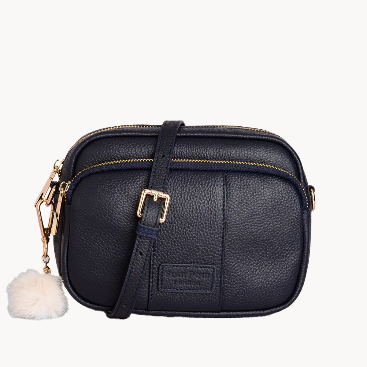 Black leather crossbody bag with gold accents and a white pom-pom on a white background