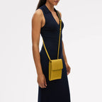 Woman wearing a navy dress with a yellow crossbody bag on a white background