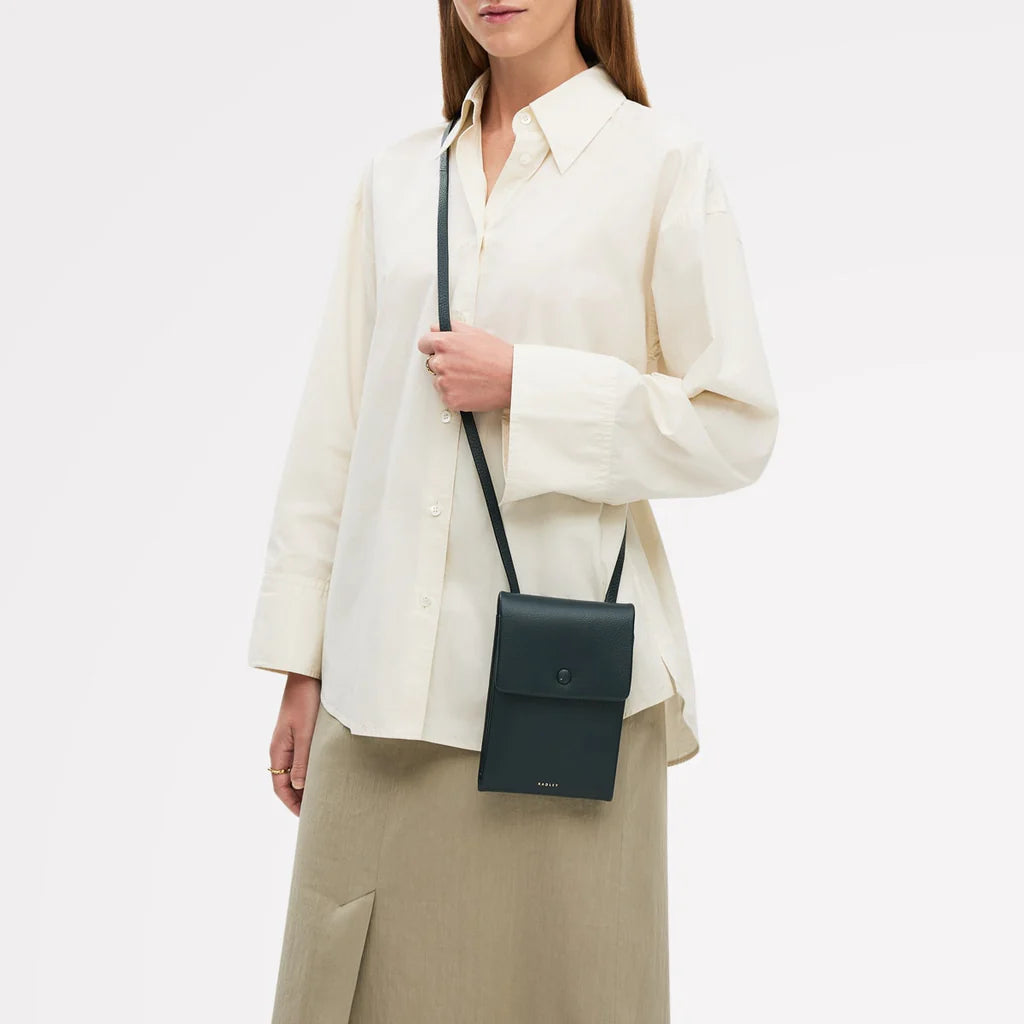 Person wearing a white shirt and beige pants with a black crossbody bag on a light gray background