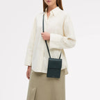 Person wearing a white shirt and beige pants with a black crossbody bag on a light gray background