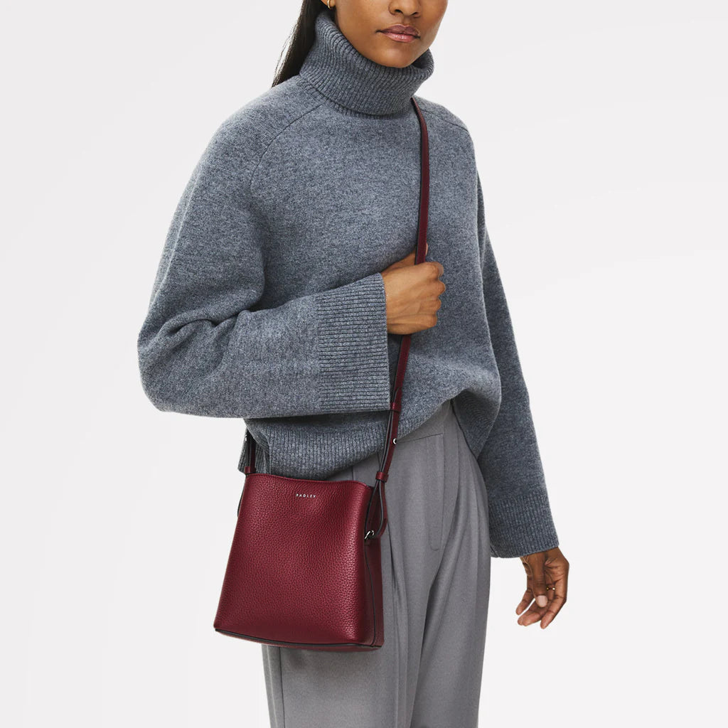 Person wearing a gray sweater and holding a red handbag on a white background