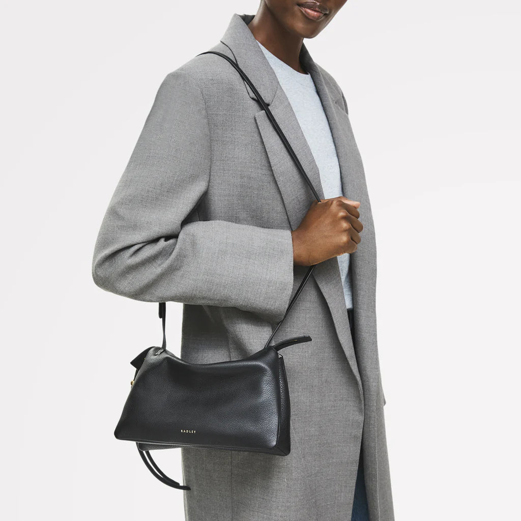 Person wearing a gray coat holding a black handbag on a white background