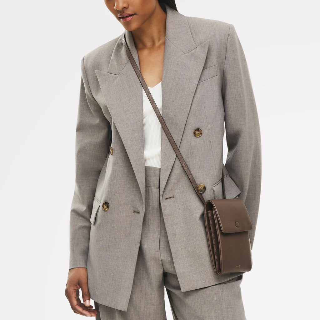 Person wearing a gray suit with a white top and carrying a brown bag on a light gray background