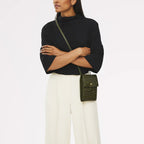 Woman wearing a black sweater and white pants with a green handbag on a white background