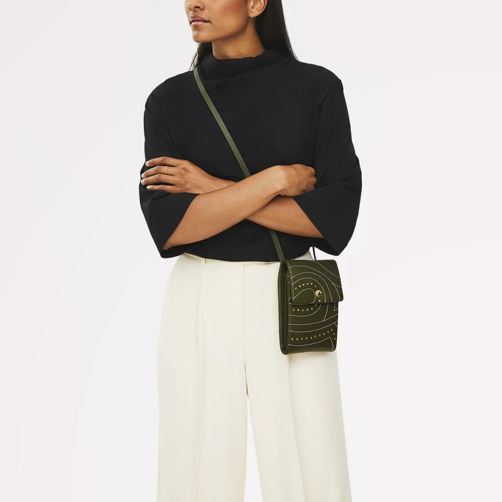 Woman wearing a black sweater and white pants with a green handbag on a white background