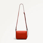 Red handbag with a brown strap on a light gray background