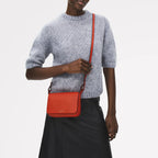 Person wearing a gray sweater and black skirt holding an orange crossbody bag on a white background