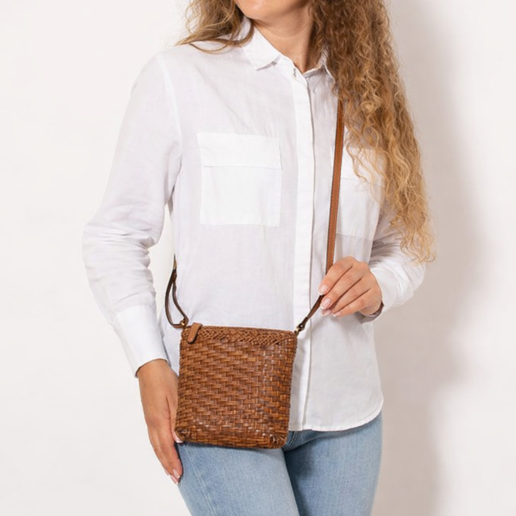 Person wearing a white shirt and holding a brown woven handbag against a plain background