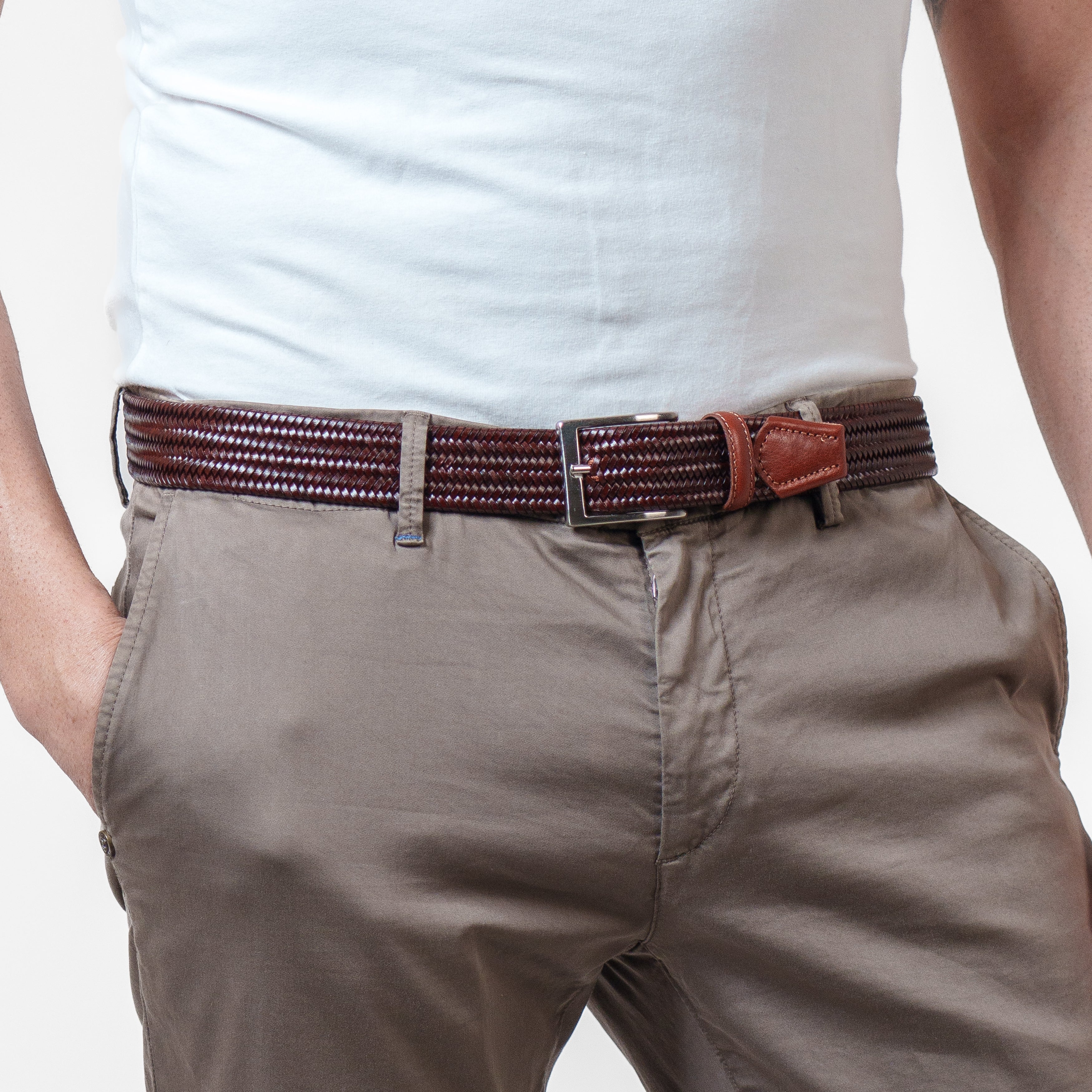 Person wearing a brown belt with a white shirt and beige pants on a light gray background