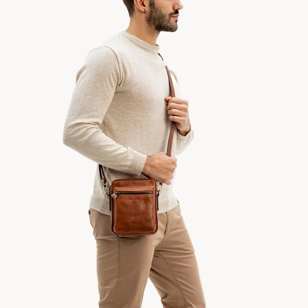 Man wearing a brown leather crossbody bag on a white background