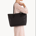 Black tote bag held by a person wearing a lace top on a white background
