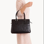 Black handbag held by a person wearing a light-colored lace dress on a white background