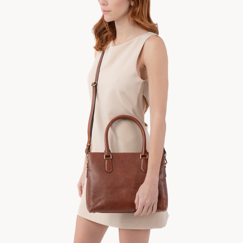 Woman holding a brown leather handbag against a white background