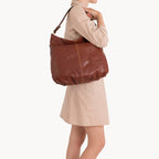 Person holding a brown leather handbag on a white background