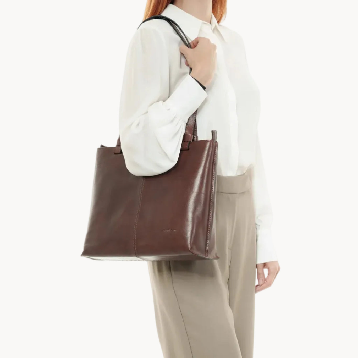 Person holding a brown leather tote bag against a white background