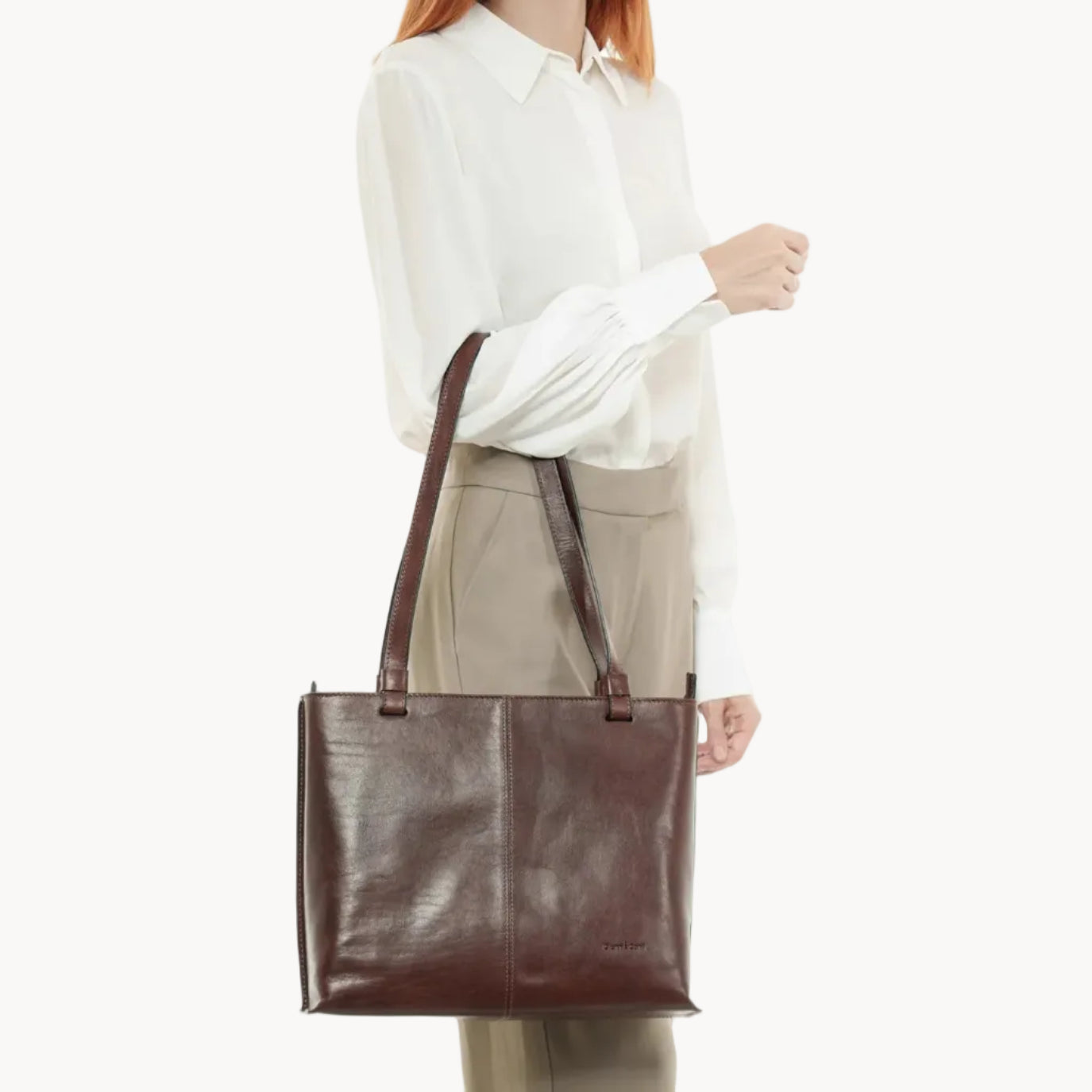 Person holding a brown leather tote bag on a white background