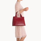 Red handbag held by a person wearing a light pink dress on a white background