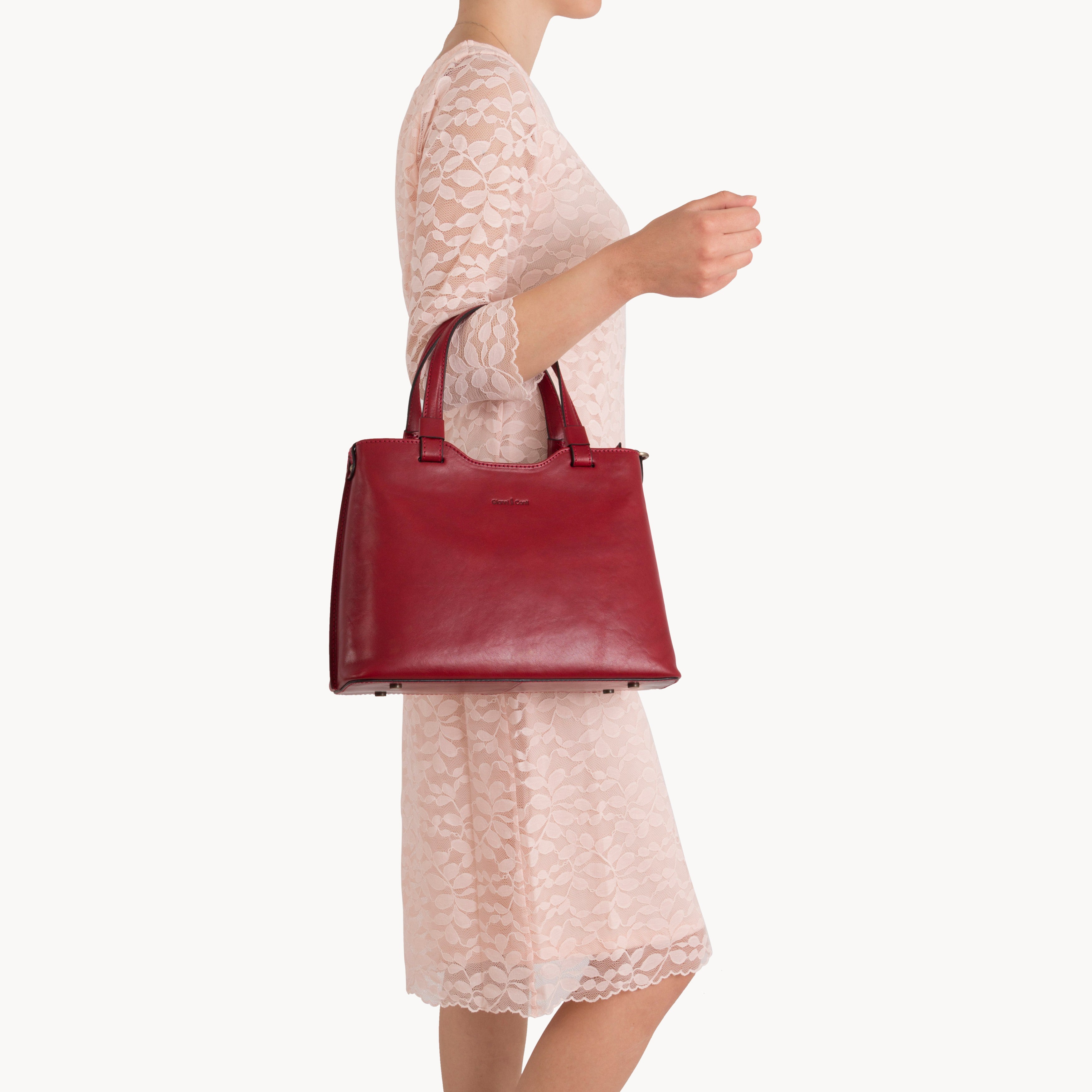 Red handbag held by a person wearing a light pink dress on a white background