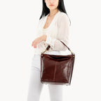 Woman holding a brown leather handbag against a white background