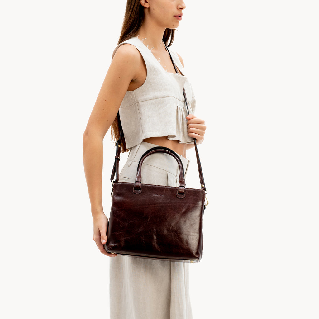 Woman holding a brown leather handbag against a white background