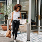 Woman walking outside a building, holding a phone and a brown handbag with a black belt bag around her waist.