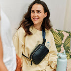 Woman wearing a black crossbody bag and holding a light blue water bottle, sitting on a couch.