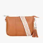 Tan leather crossbody bag with a patterned strap and tassel on a white background