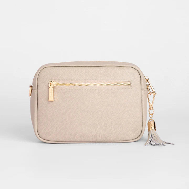 Beige crossbody bag with gold zipper and tassel on a light gray background