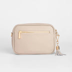 Beige crossbody bag with gold zipper and tassel on a light gray background