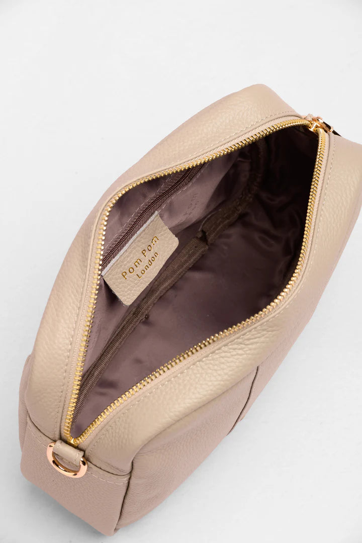 Beige crossbody bag with gold zipper and visible brand label on a light gray background