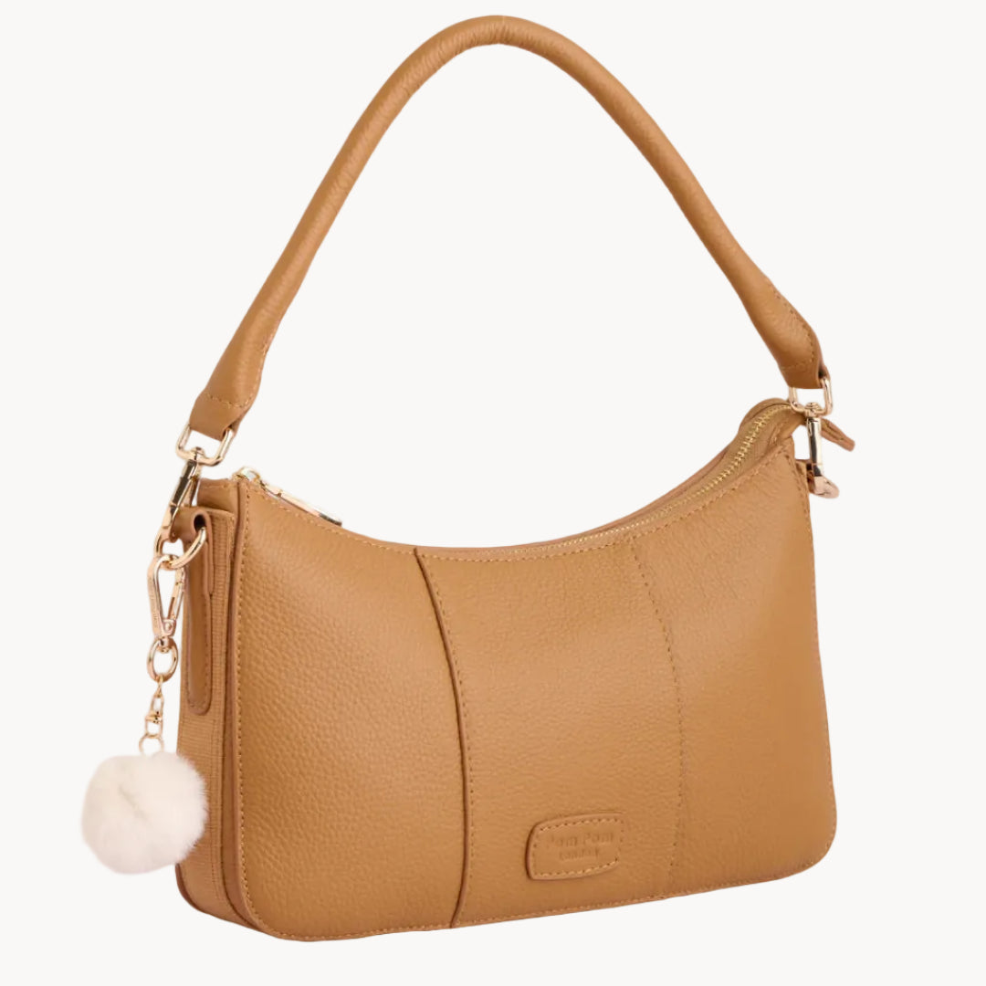 Tan handbag with a pom-pom charm on a light gray background