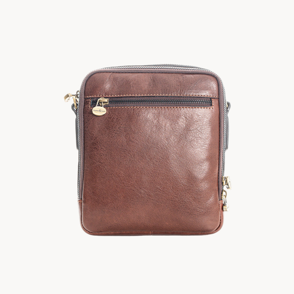 Brown leather crossbody bag with gold zipper pulls on a white background