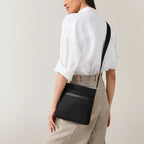 Person wearing a black crossbody bag on a plain background