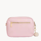 Pink handbag with gold zipper and pom-pom detail on a gray background