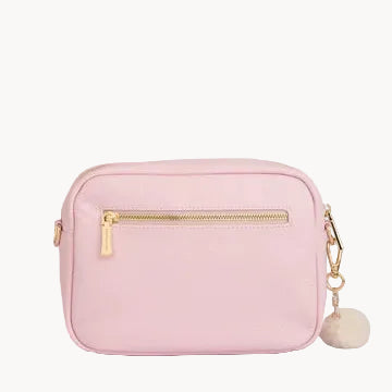 Pink handbag with gold zipper and pom-pom detail on a gray background
