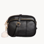 Black leather crossbody bag with a white pom-pom on a white background