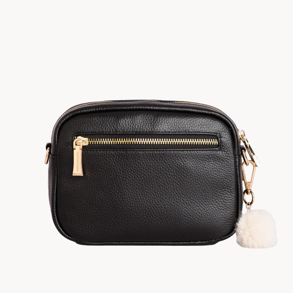 Black leather crossbody bag with gold zipper and white pom-pom on a white background