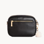 Black leather crossbody bag with gold zipper and white pom-pom on a white background