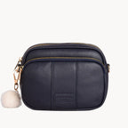 Black leather crossbody bag with a fluffy pom-pom on a white background