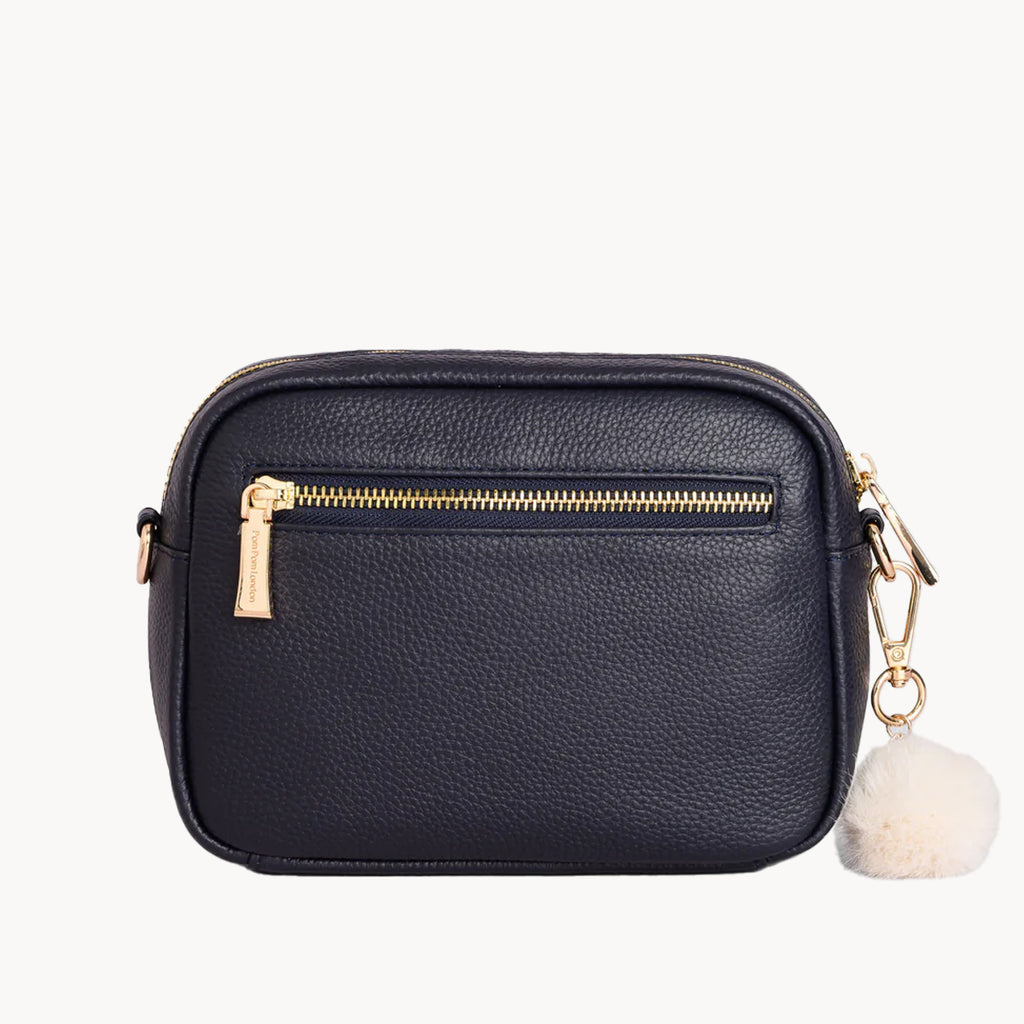 Black crossbody bag with gold zipper and white pom-pom charm on a white background