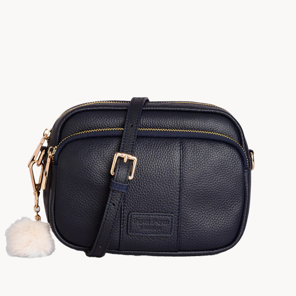 Black leather crossbody bag with gold accents and a white pom-pom on a white background