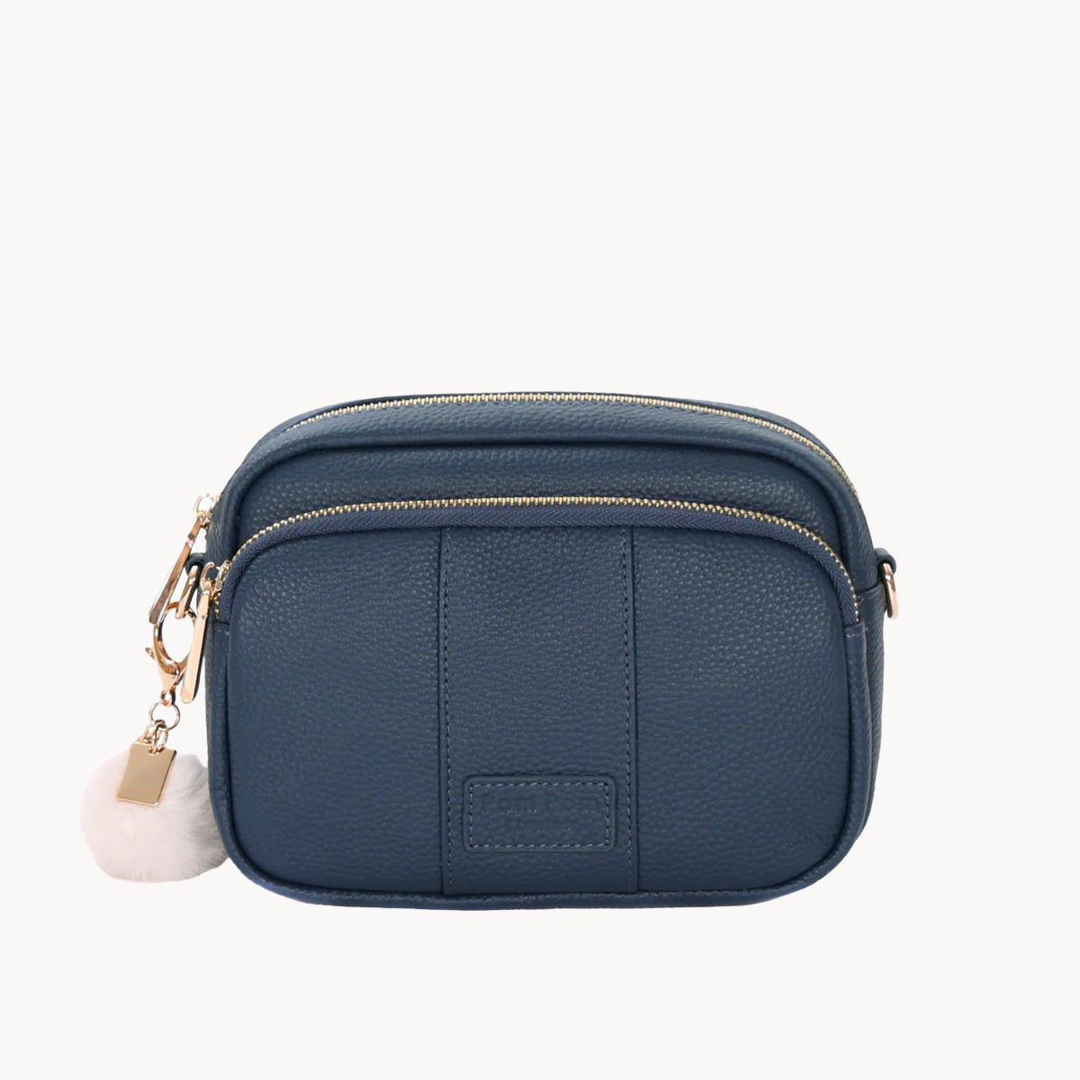 Navy blue crossbody bag with a gold zipper and white pom-pom charm on a white background