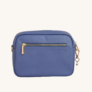 Blue leather crossbody bag with gold zipper and decorative charm on a light gray background