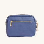 Blue leather crossbody bag with gold zipper and decorative charm on a light gray background