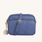 Blue crossbody bag with a pom-pom charm on a light gray background