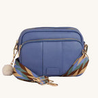 Blue crossbody bag with a patterned strap on a gray background